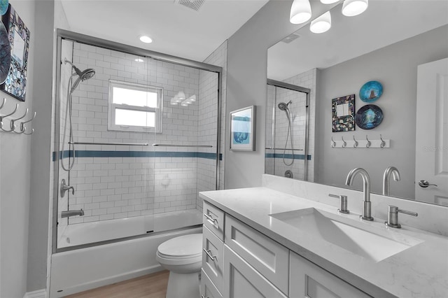 full bathroom featuring wood-type flooring, vanity, combined bath / shower with glass door, and toilet