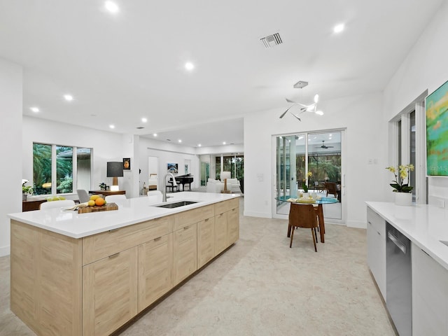 kitchen featuring stainless steel dishwasher, a kitchen island with sink, sink, and light brown cabinetry