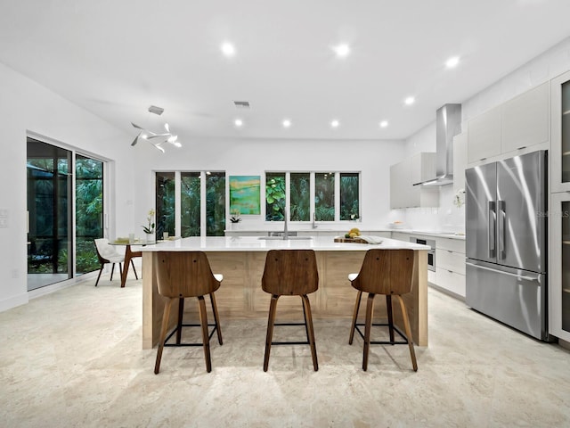 kitchen featuring appliances with stainless steel finishes, a large island, a breakfast bar area, and wall chimney range hood