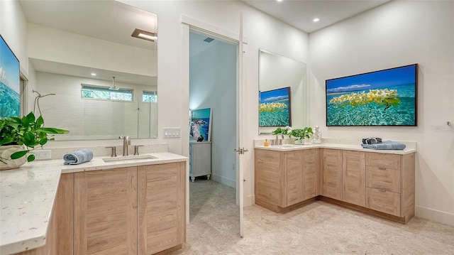 full bath featuring baseboards, two vanities, a sink, and tiled shower