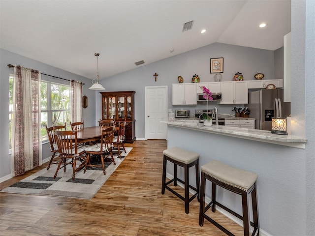 kitchen featuring white cabinets, appliances with stainless steel finishes, lofted ceiling, kitchen peninsula, and light wood-type flooring