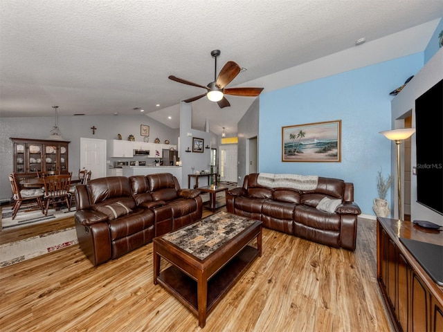 living room with light wood-type flooring, vaulted ceiling, ceiling fan, and a textured ceiling