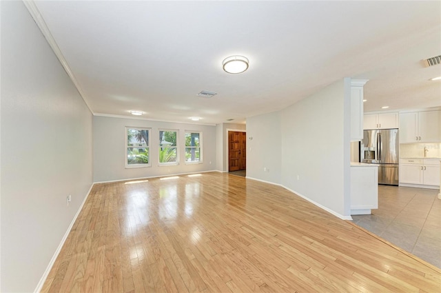 unfurnished living room featuring ornamental molding, baseboards, visible vents, and light wood finished floors