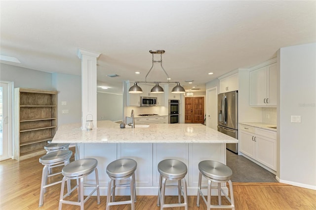 kitchen with light stone counters, stainless steel appliances, hanging light fixtures, white cabinets, and light wood-type flooring