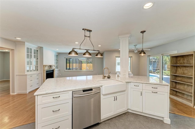 kitchen with a center island with sink, hanging light fixtures, stainless steel dishwasher, white cabinetry, and a sink