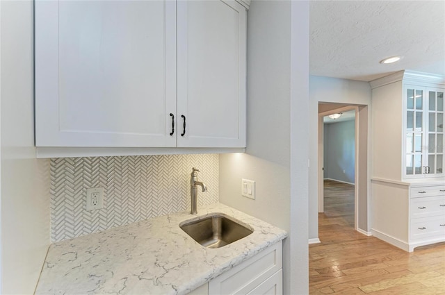 kitchen featuring light stone counters, a sink, and white cabinets