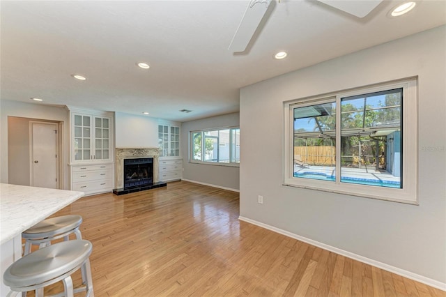 unfurnished living room with recessed lighting, light wood-style flooring, a ceiling fan, a high end fireplace, and baseboards