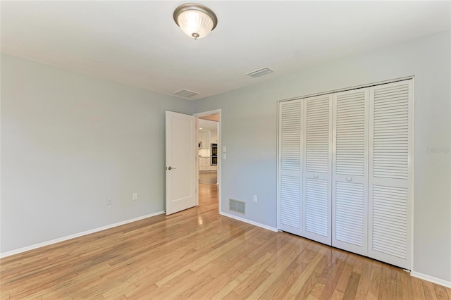 unfurnished bedroom featuring light wood-type flooring, visible vents, baseboards, and a closet