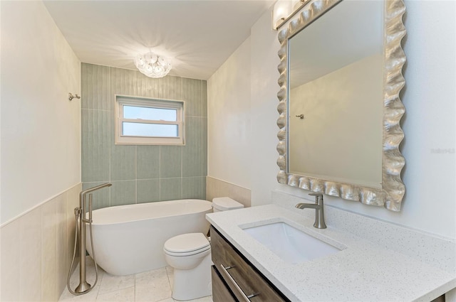 full bath with a freestanding bath, toilet, wainscoting, vanity, and tile patterned floors