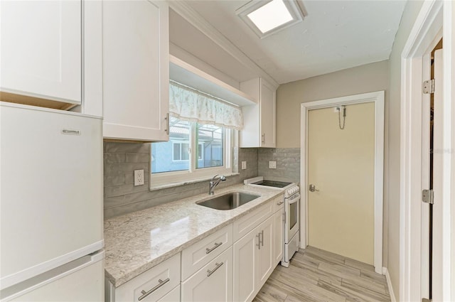 kitchen featuring white appliances, tasteful backsplash, white cabinets, light stone counters, and a sink