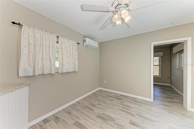 unfurnished room with baseboards, a wall unit AC, ceiling fan, and light wood finished floors