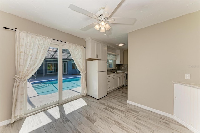 interior space with a ceiling fan, light wood-type flooring, a sink, and baseboards