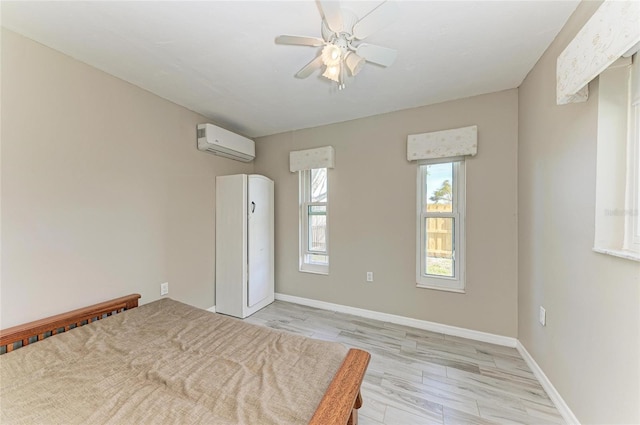 unfurnished bedroom featuring an AC wall unit, baseboards, ceiling fan, and light wood finished floors