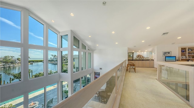 hall featuring a water view, light colored carpet, and high vaulted ceiling