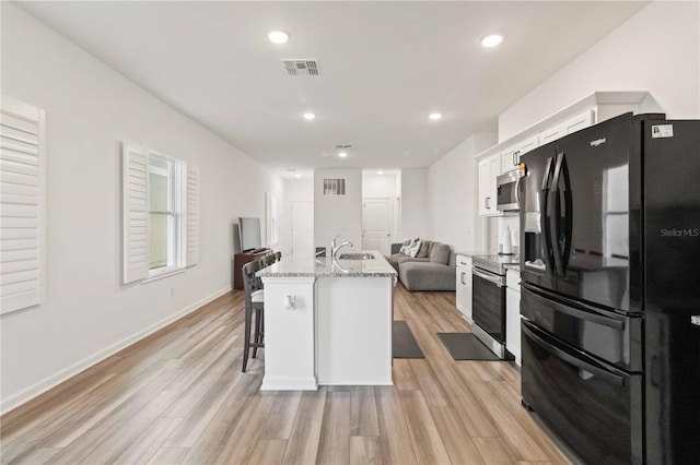 kitchen featuring a kitchen breakfast bar, white cabinetry, a kitchen island with sink, stainless steel appliances, and light hardwood / wood-style flooring