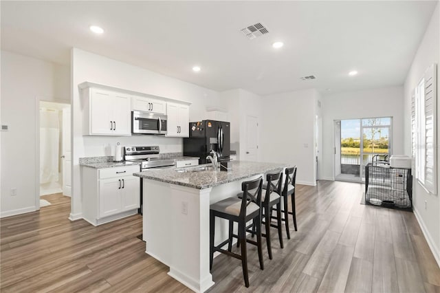 kitchen with white cabinetry, light stone counters, a kitchen bar, an island with sink, and appliances with stainless steel finishes