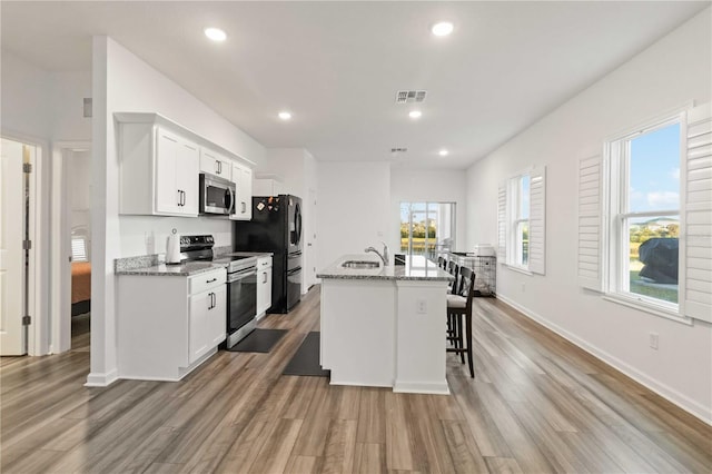 kitchen featuring stainless steel appliances, a center island with sink, light stone countertops, and white cabinetry