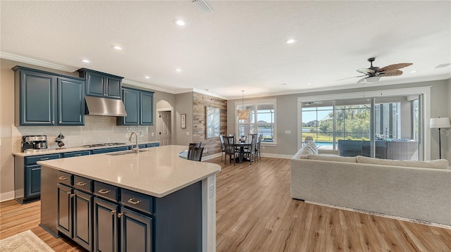 kitchen featuring a center island with sink, ceiling fan, light wood-type flooring, crown molding, and sink