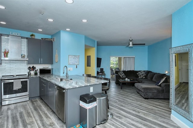 kitchen featuring kitchen peninsula, appliances with stainless steel finishes, light stone countertops, wall chimney exhaust hood, and ceiling fan