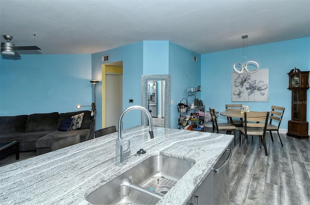 kitchen with dishwasher, sink, hardwood / wood-style flooring, ceiling fan, and light stone counters