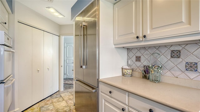 kitchen with white cabinetry, backsplash, white double oven, and built in refrigerator