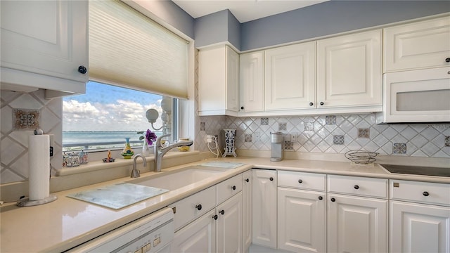 kitchen featuring tasteful backsplash, white cabinetry, sink, a water view, and white appliances