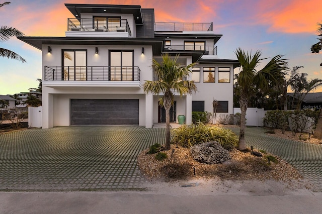 view of front facade with stucco siding, decorative driveway, a balcony, and fence