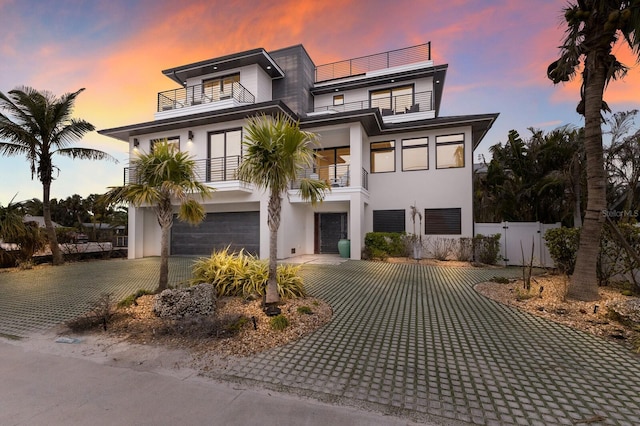 modern home featuring a gate, decorative driveway, fence, a garage, and a balcony