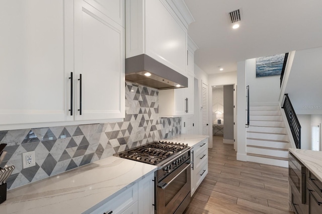 kitchen with white cabinets, light stone counters, extractor fan, and high end stove