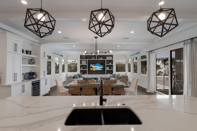 kitchen featuring decorative light fixtures, beam ceiling, beverage cooler, and light stone counters