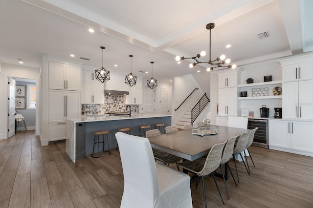 dining room featuring wine cooler, indoor bar, beamed ceiling, and light hardwood / wood-style floors