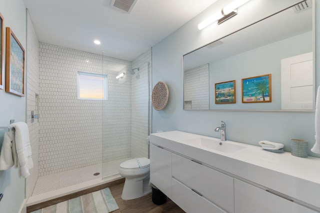 bathroom with toilet, vanity, wood-type flooring, and tiled shower