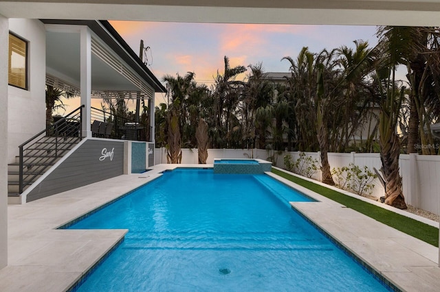 pool at dusk featuring an in ground hot tub and a patio