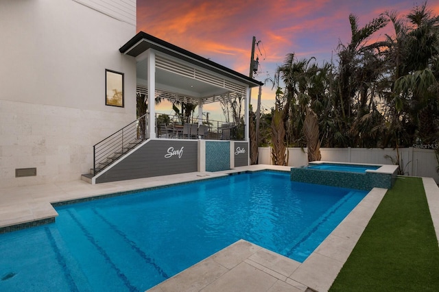 pool at dusk with an in ground hot tub and a patio