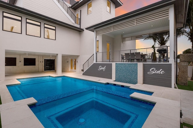 pool at dusk featuring a patio area and an in ground hot tub