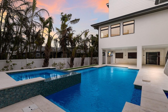 pool at dusk featuring a patio area and an in ground hot tub