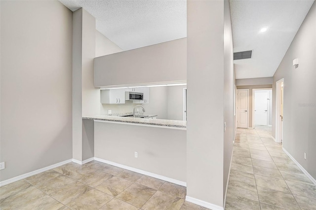 kitchen with light tile patterned floors, stove, lofted ceiling, light stone countertops, and white cabinets