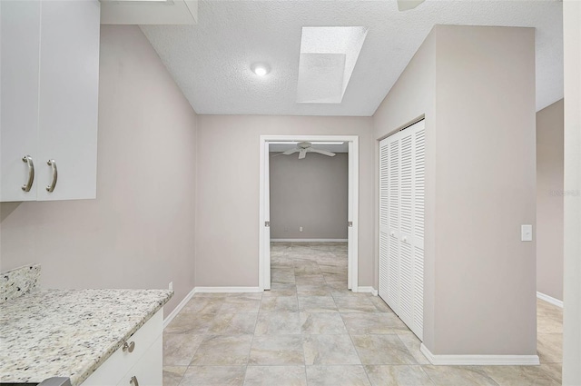 interior space with a textured ceiling, ceiling fan, and a skylight