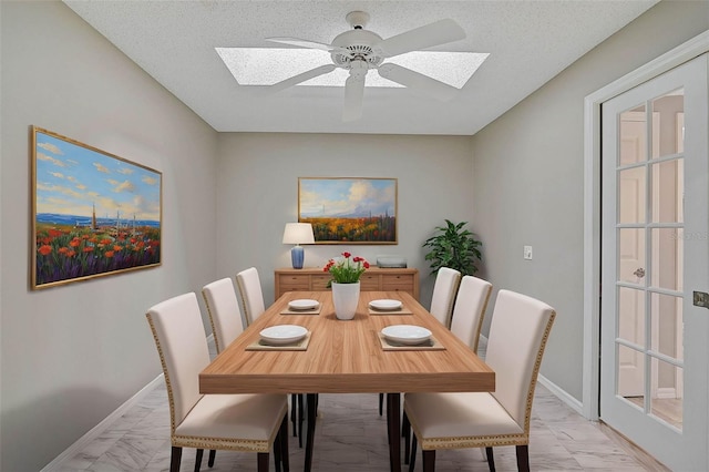 dining area featuring ceiling fan, a textured ceiling, and a skylight