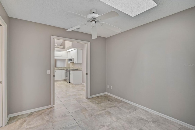 empty room featuring ceiling fan, a skylight, and a textured ceiling