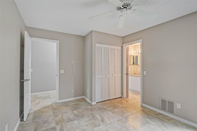 unfurnished bedroom featuring a textured ceiling, ceiling fan, ensuite bathroom, and a closet