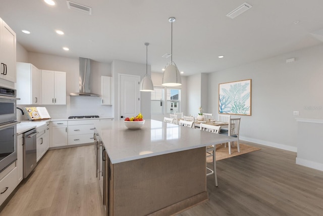 kitchen with gas stovetop, stainless steel dishwasher, white cabinets, a kitchen island, and wall chimney exhaust hood