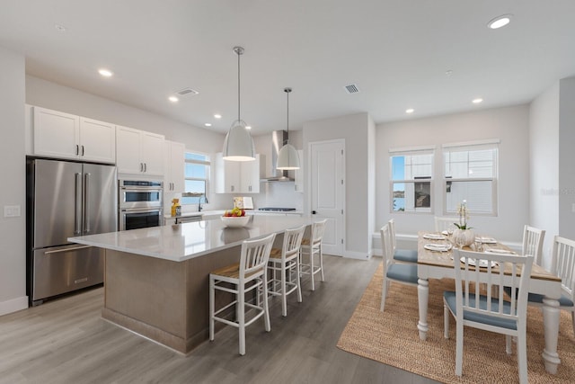 kitchen featuring white cabinetry, stainless steel appliances, a kitchen island, and wall chimney exhaust hood