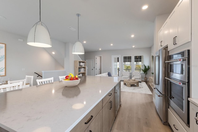 kitchen with pendant lighting, a large island, white cabinetry, light stone countertops, and a breakfast bar