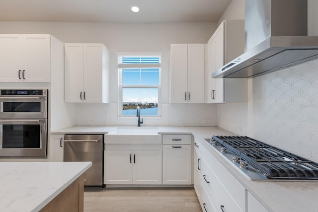 kitchen with wall chimney exhaust hood, white cabinets, tasteful backsplash, and stainless steel appliances