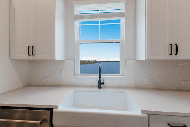 kitchen with sink, white cabinets, light stone countertops, and stainless steel dishwasher