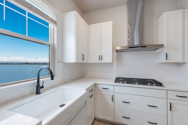 kitchen featuring white cabinets, wall chimney range hood, sink, a water view, and stainless steel gas stovetop