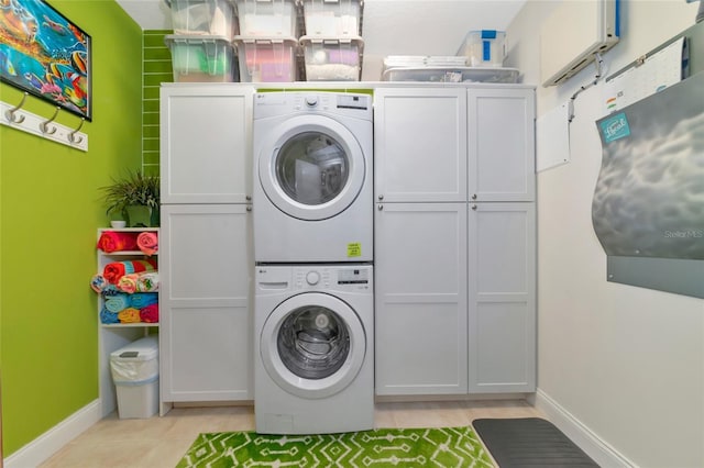 laundry area featuring stacked washer / drying machine, cabinets, and light tile patterned floors