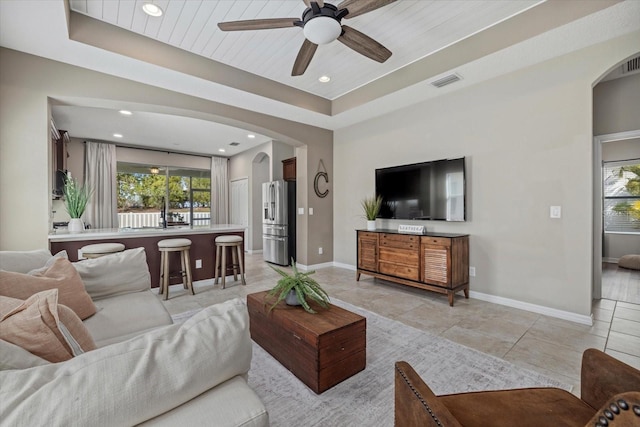 tiled living room with ceiling fan, a raised ceiling, and a wealth of natural light