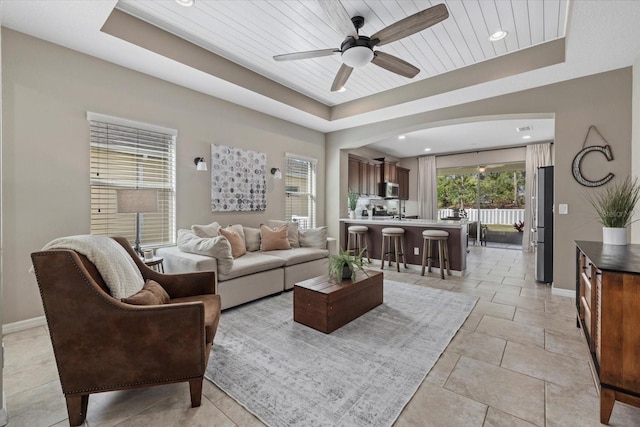 living room with ceiling fan, wood ceiling, and a raised ceiling